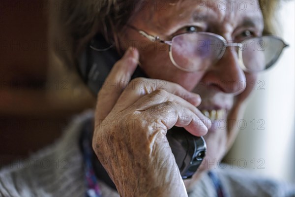 Laughing senior citizen talking on the phone at home in her living room, Cologne, North Rhine-Westphalia, Germany, Europe