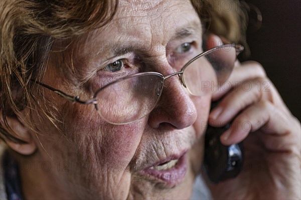 Senior citizen looks serious, frightened while talking on the phone in her living room, Cologne, North Rhine-Westphalia, Germany, Europe