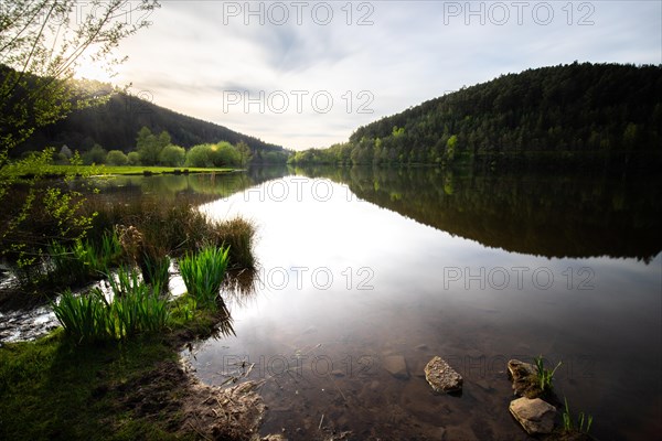 A lake in a landscape shot. A sunset and the natural surroundings are reflected in the water of the reservoir. Marbach reservoir, Odenwald, Hesse