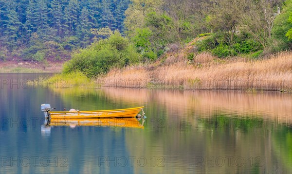 Small yellow metal fishing boat with small engine mount floating peacefully on a lake in South Korea