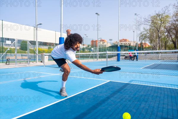 Full length photo of an african sportive man trying to reach the ball playing pickleball in an outdoor court