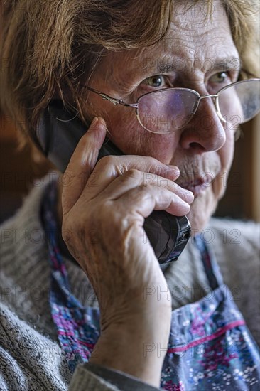 Senior citizen looks serious, frightened while talking on the phone in her living room, Cologne, North Rhine-Westphalia, Germany, Europe