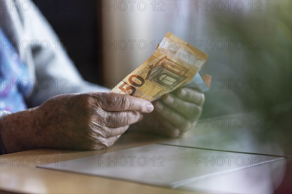 Senior citizen with wrinkled hands counts her money at home in her flat and holds banknotes in her hand, Cologne, North Rhine-Westphalia, Germany, Europe