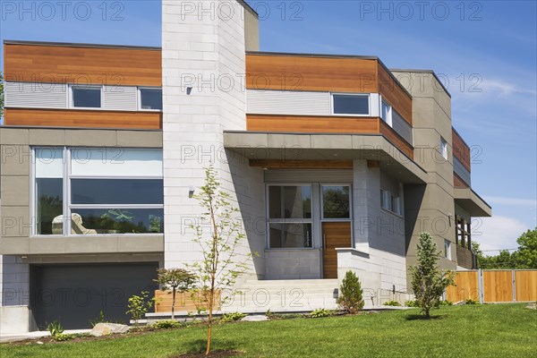 Two story grey and charcoal stone with cedar wood siding modern cube style home facade in summer, Quebec, Canada, North America