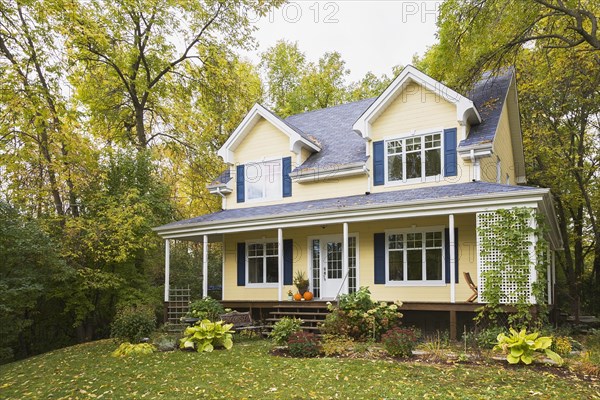Two storey yellow clapboard with blue and white trim cottage style home facade in autumn, Quebec, Canada, North America