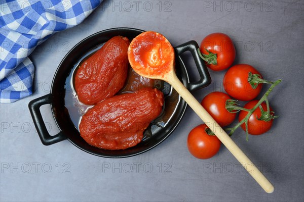 Whole tinned tomatoes in a pot, tomatoes and wooden spoon