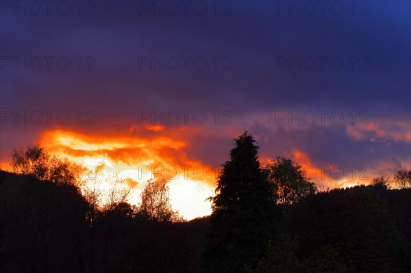 Sunset with dramitic dark clouds, sun shining through a gap in the clouds, red sky, burning sky, silhouette, Rothaargebirge, North Rhine-Westphalia, Germany, Europe