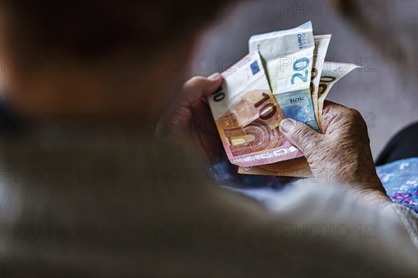 Senior citizen with wrinkled hands counts her money at home in her flat and holds banknotes in her hand, Cologne, North Rhine-Westphalia, Germany, Europe