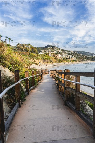 A wooden boardwalk leads to the beach. The boardwalk has a railing. Vertical shot