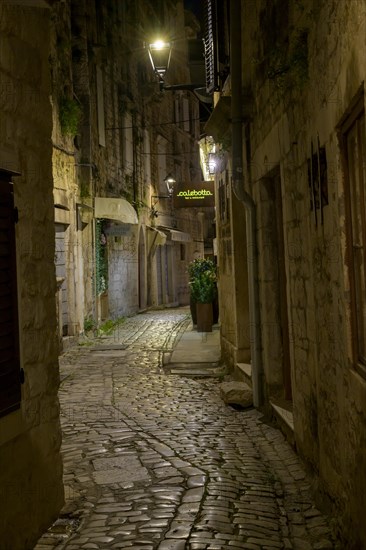 Night scene of a narrow alley with cobblestone floor and illuminated signs on the buildings, Trogir, Dalmatia, Croatia, Europe