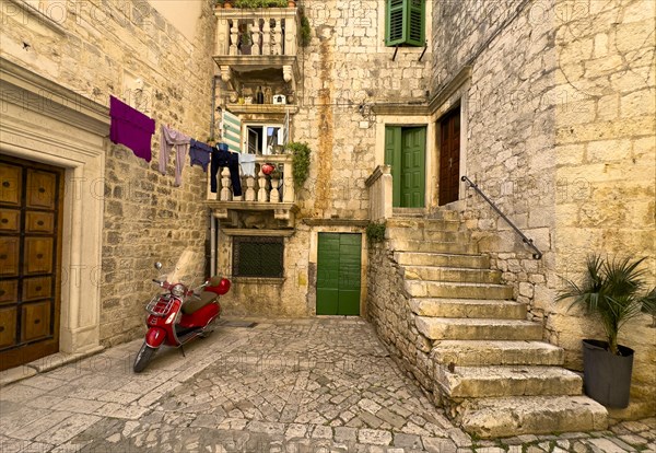 Laundry hanging over an alley with a red Vespa and green shutters, Trogir, Dalmatia, Croatia, Europe