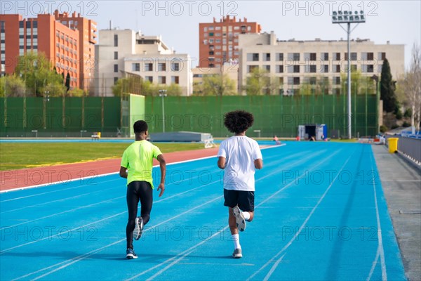 Full length rear view of two sportive african men running in an athletics track