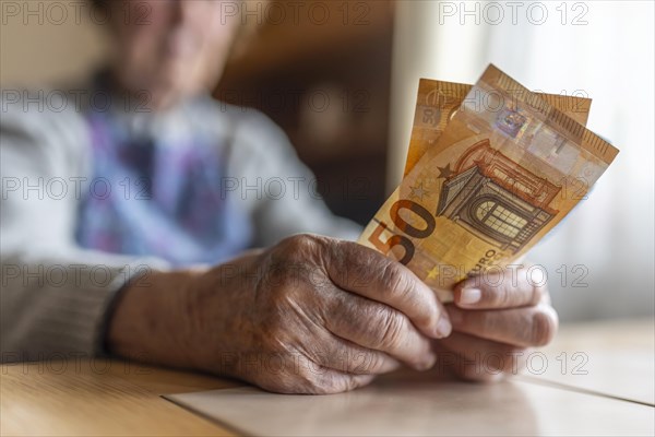 Senior citizen with wrinkled hands counts her money at home in her flat and holds banknotes in her hand, Cologne, North Rhine-Westphalia, Germany, Europe