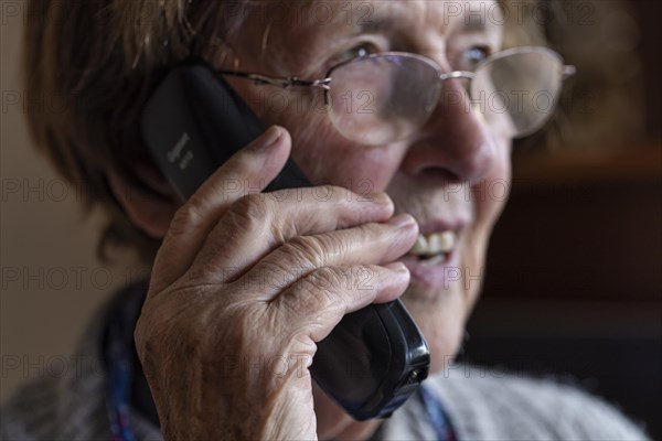 Laughing senior citizen with smock talking on the phone at home in her living room, Cologne, North Rhine-Westphalia, Germany, Europe