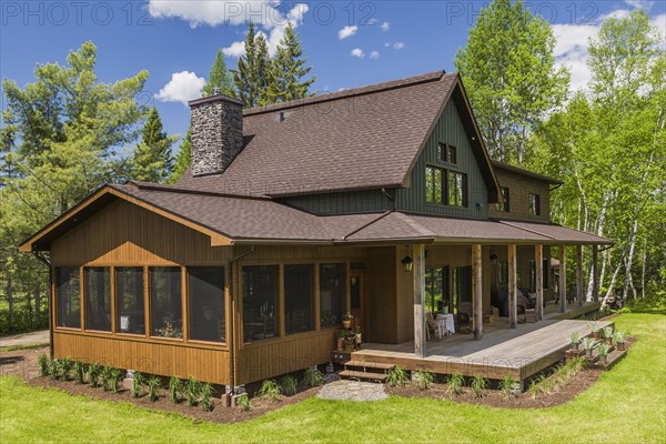 Elevated rear view of brown and green stained spruce wood and cedar shingle siding LEED certified Country home with veranda in late spring, Quebec, Canada, North America