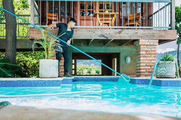 Man cleaning swimming pool water with a skimmer. Maintenance person cleaning the leaves of a pool with the skimmer
