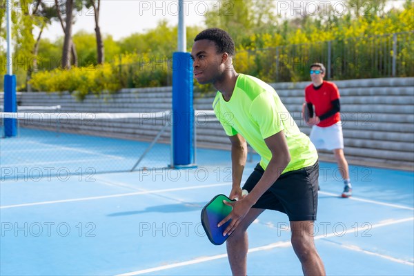 Multi-ethnic friends playing pickleball together in a sunny day in an outdoor blue court