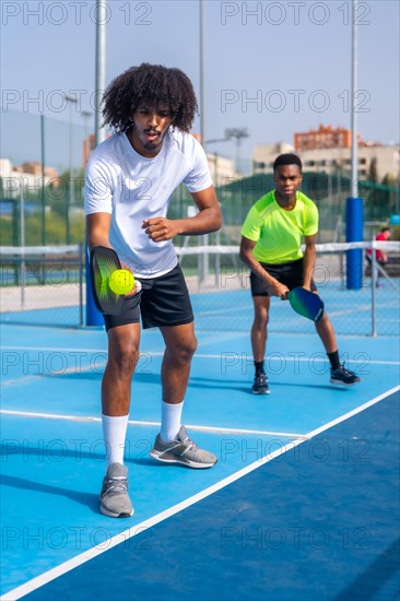 Vertical full length photo of an african sportive man serving ball during pickleball match outdoors