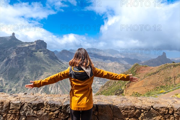A tourist woman looking at Roque Nublo from a viewpoint with her arms open. Gran Canaria, Spain, Europe