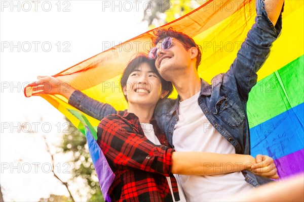 Low angle view of a multi-ethnic gay couple celebrating diversity raising lgbt flag in a park