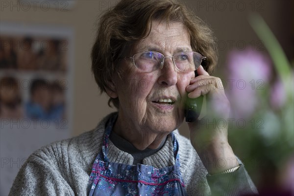 Senior citizen looks serious, frightened while talking on the phone in her living room, Cologne, North Rhine-Westphalia, Germany, Europe