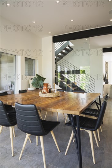 American walnut wood dining table and black leather sitting chairs with ash wood legs in dining room inside modern cube style home, Quebec, Canada, North America