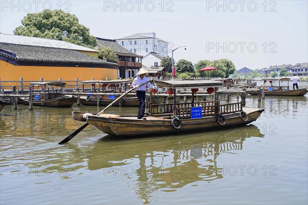 Excursion to Zhujiajiao water village, Shanghai, China, Asia, wooden boat on canal with view of historical architecture, person rowing a wooden boat along a river near a wooden jetty and buildings, Asia