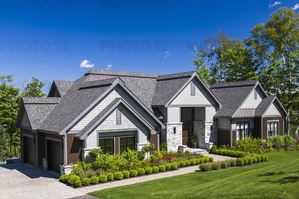 Contemporary natural stone and brown stained wood and cedar shingles clad luxurious bungalow style home facade in summer, Quebec, Canada, North America