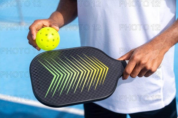 Unrecognizable close-up sportive man with pickleball equipment holding racket and yellow ball in an court