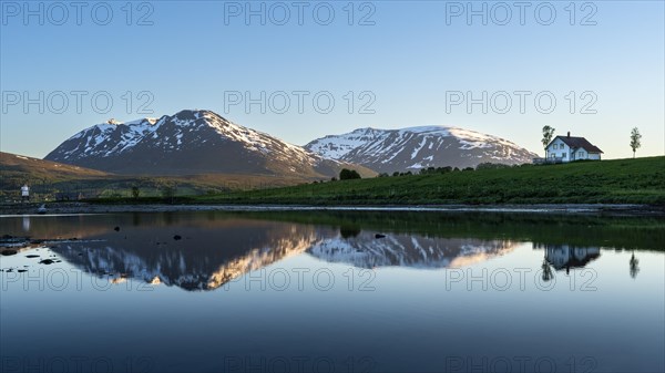 Landscape in Norway. The Balsfjord with a view of mountains and a house by the sea. At night at the time of the midnight sun, good weather, blue sky. Early summer. Reflection. Laksvatn, Troms, Norway, Europe