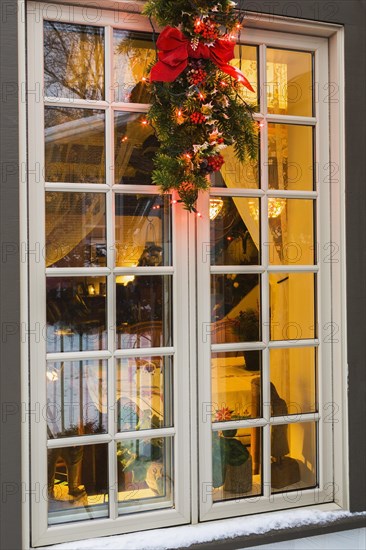 Brown and beige window with illuminated Christmas lights and decorations on an old circa 1886 white with beige and brown trim Canadiana cottage style home at dusk in winter, Quebec, Canada, North America