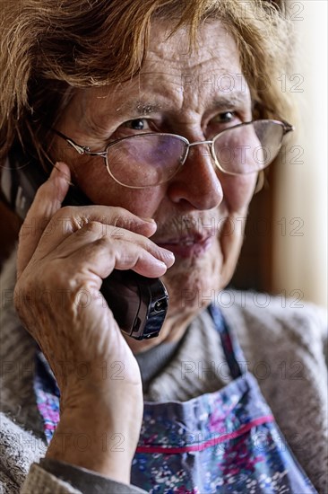 Laughing senior citizen with smock talking on the phone at home in her living room, Cologne, North Rhine-Westphalia, Germany, Europe