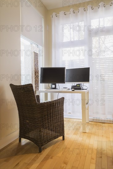 Brown high-back wicker chair and white desk table with computer in home office in master bedroom inside a renovated ground floor apartment in an old residential cottage style home, Quebec, Canada, North America