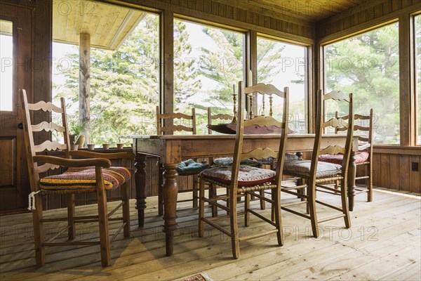 Sun room with antique wooden harvest dining table and chairs, treated wood floorboards inside a LEED certified Country home, Quebec, Canada, North America
