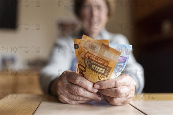 Senior citizen with wrinkled hands counts her money at home in her flat and holds banknotes in her hand, Cologne, North Rhine-Westphalia, Germany, Europe