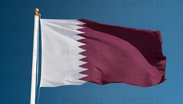 The flag of Qatar flutters in the wind, isolated against a blue sky