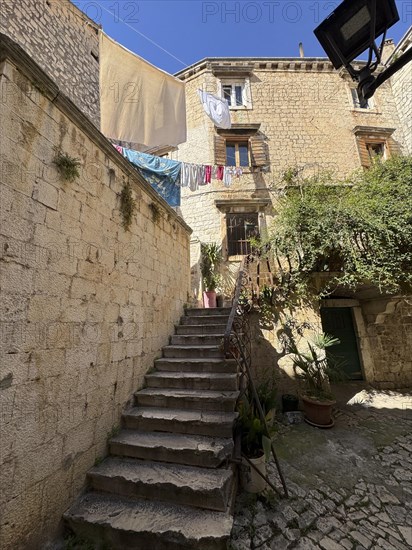 Stone staircase in a sunny alleyway of the old town centre with hanging laundry, Trogir, Dalmatia, Croatia, Europe
