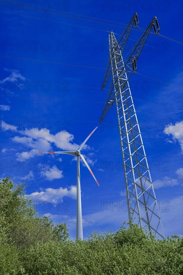 Power pylon with high-voltage lines and wind turbine behind green trees at the Avacon substation Helmstedt, Helmstedt, Lower Saxony, Germany, Europe