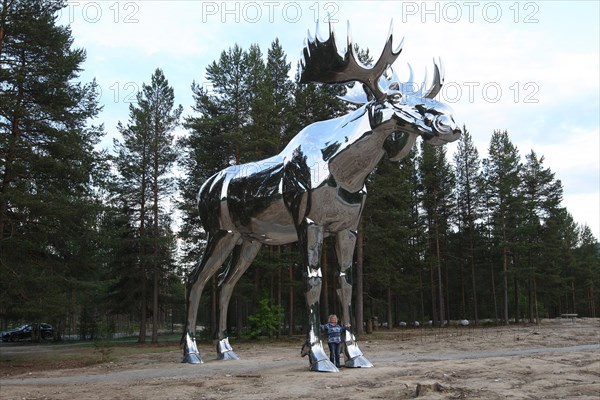 Elk (Alces alces) 10 metres high is the world's largest moose made of polished steel, between Oslo and central Norway, the tourist between its legs looks dwarfed, central Norway, Scandinavia
