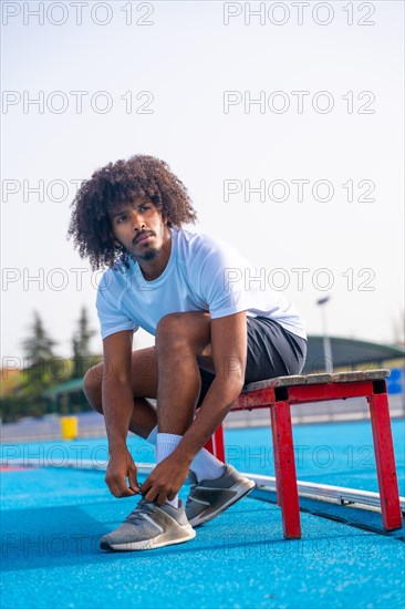 Vertical portrait of a concentrated young african american running getting ready to train tying her shoelaces in a blue outdoor running track