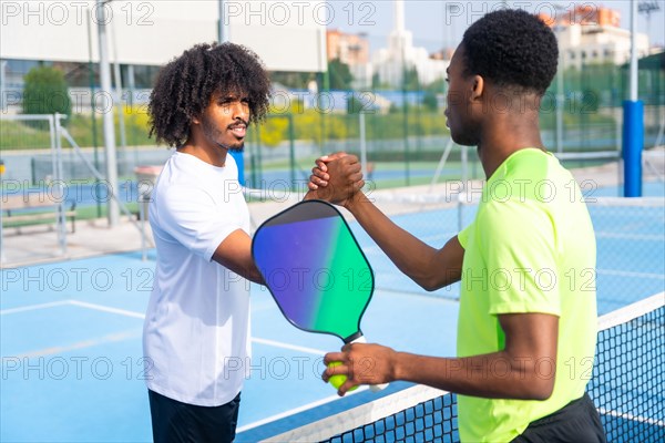 Two african american young men shaking hands before playing pickleball in an outdoor court