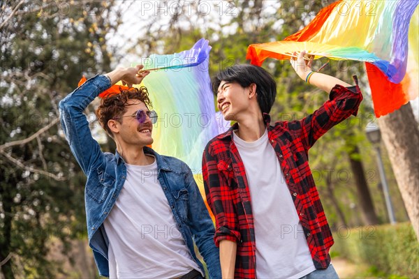 Gay couple holding hands strolling happily in a park raising lgbt rainbow hand fans