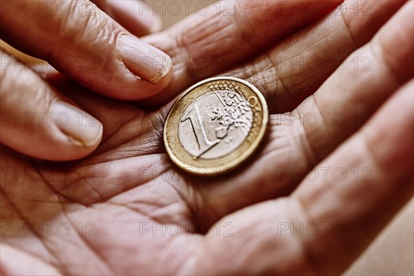 A euro coin in the wrinkled hand of a senior citizen, symbolising poverty and poverty in old age