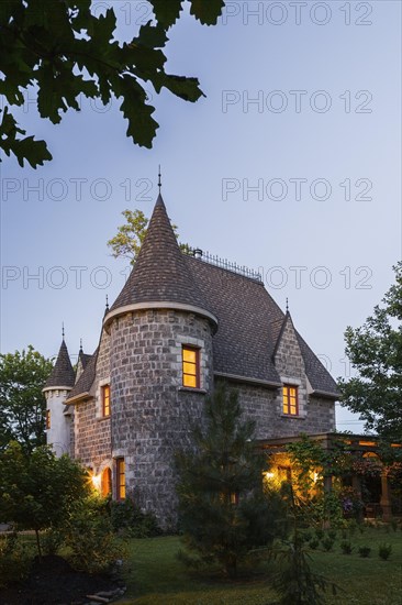 2006 reproduction of a 16th century grey stone and mortar Renaissance castle style residential home facade at dusk in summer, Quebec, Canada, North America
