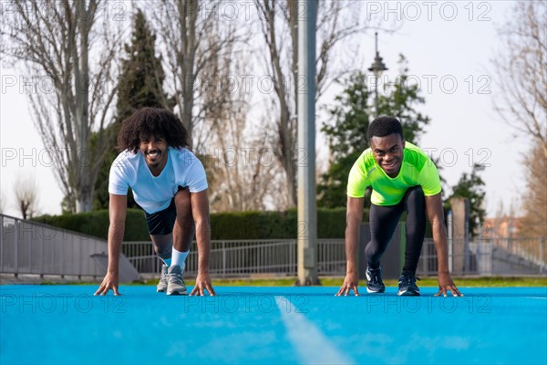 Frontal view of two sportive young african males in position to start a race in a blue running track