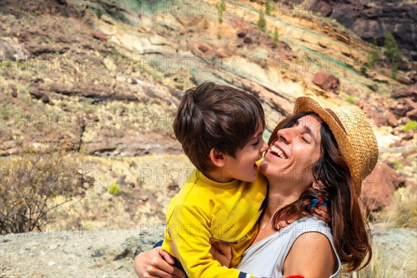 A woman and a child are hugging in a field. The woman is wearing a straw hat. Scene is warm and loving