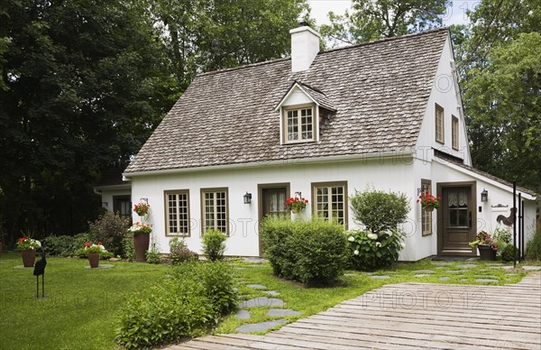 Old circa 1886 white with beige and brown trim Canadiana cottage style home facade with wood plank driveway in summer, Quebec, Canada, North America