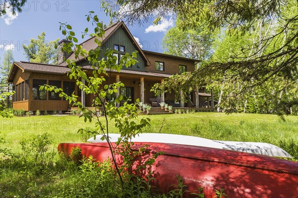 Rear view of brown and green stained spruce wood and cedar shingle siding LEED certified Country home with veranda in late spring, Quebec, Canada, North America