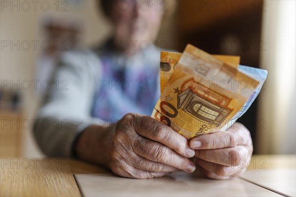 Senior citizen with wrinkled hands counts her money at home in her flat and holds banknotes in her hand, Cologne, North Rhine-Westphalia, Germany, Europe