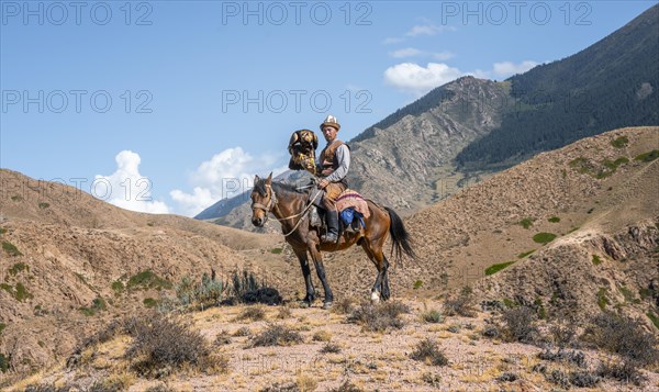 Traditional Kyrgyz eagle hunter riding with eagle in the mountains, hunting on horseback, near Bokonbayevo, Issyk Kul region, Kyrgyzstan, Asia